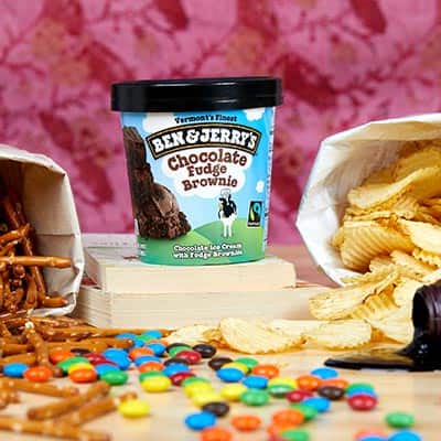 A pint of ice cream, pretzels, potato chips and candy on desk